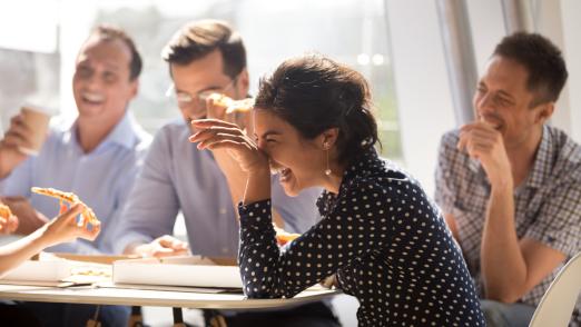 Indian woman laughing eating pizza with diverse coworkers in off